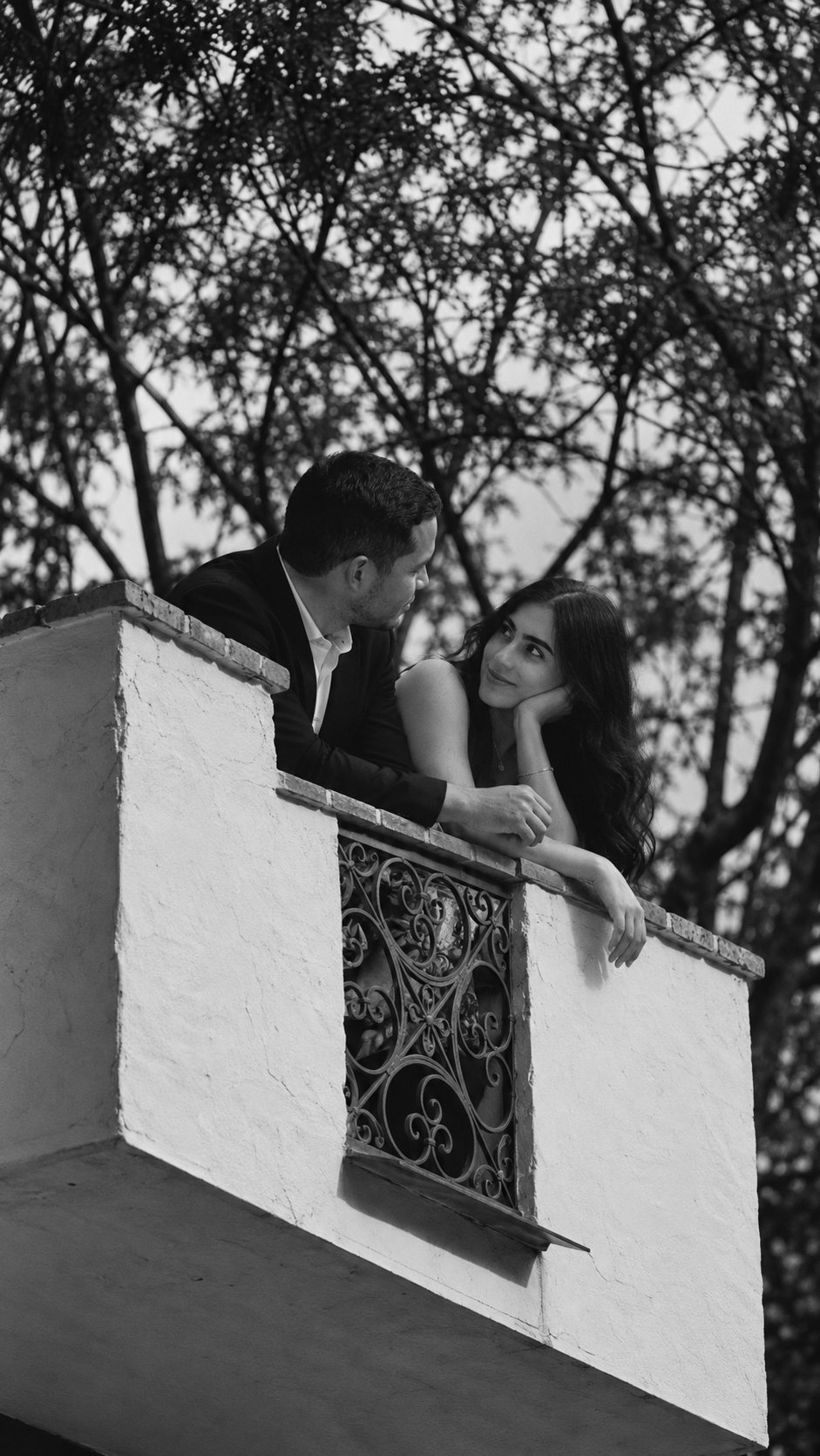 Laura and Cristian leaning on a white balcony wall, smiling at each other